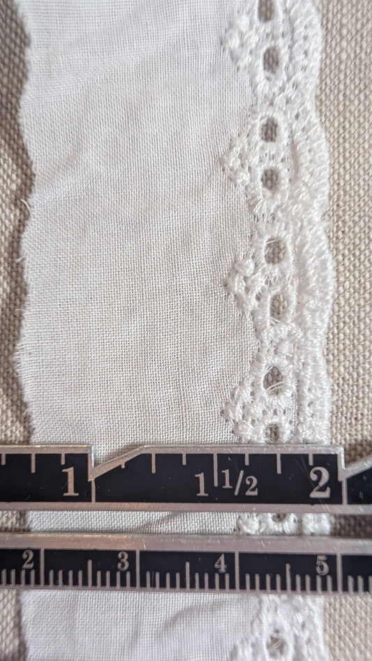 Close-up of Martha Pullen cotton Swiss embroidery lace trim with a ruler for scale on a textured fabric background