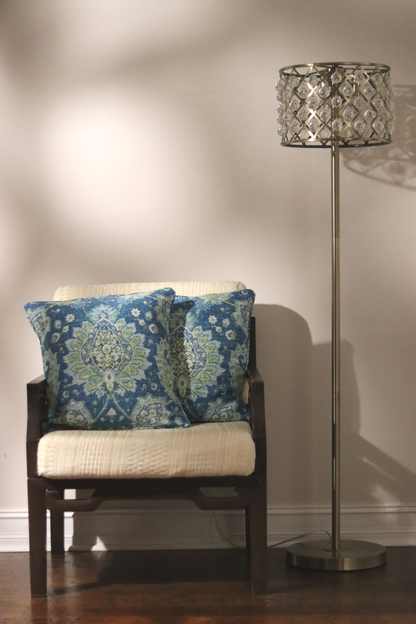Chair with blue and green print throw pillow cover  next to a floor lamp