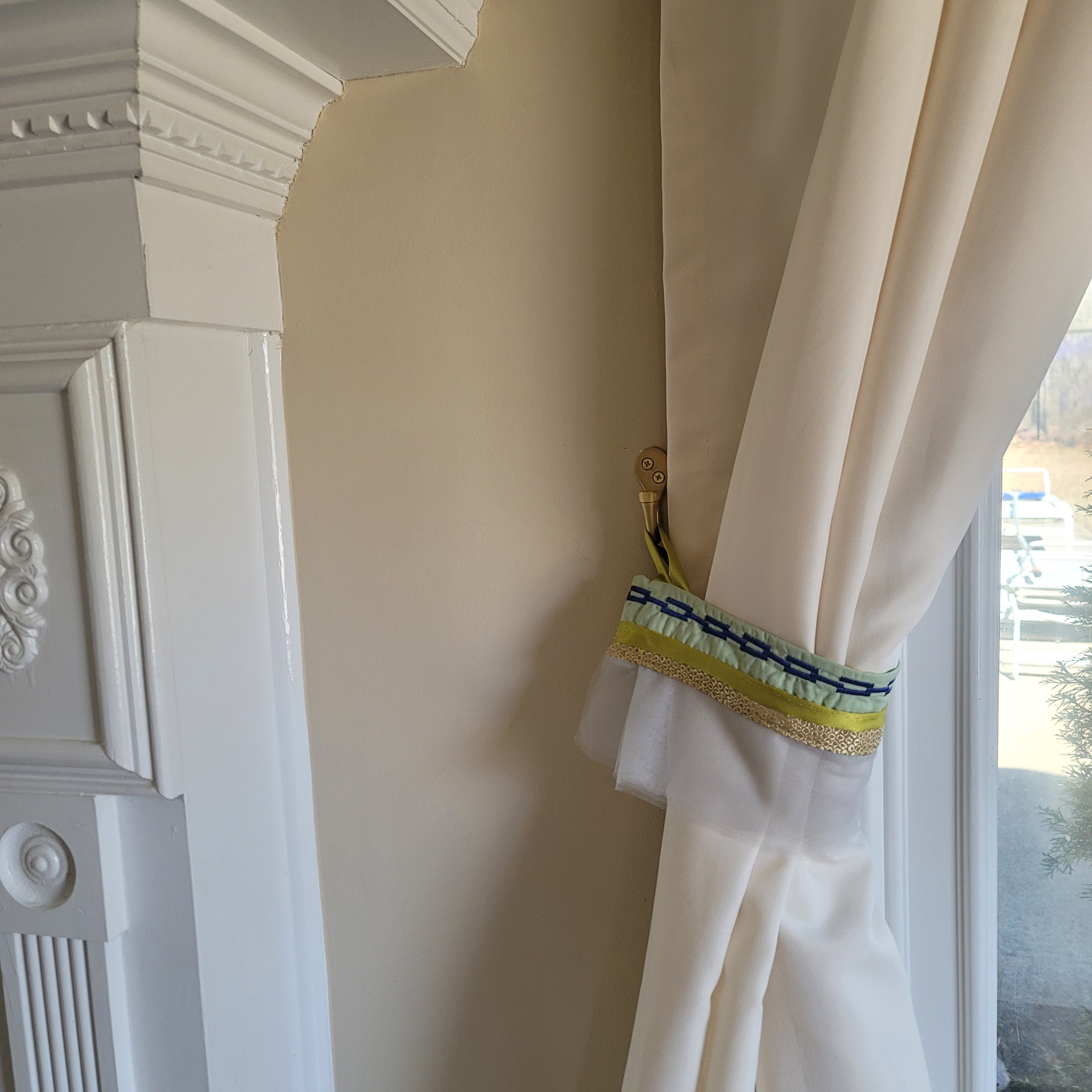 Cream curtain hold by tieback in green and tulle fabric with blue decorative chain stitch