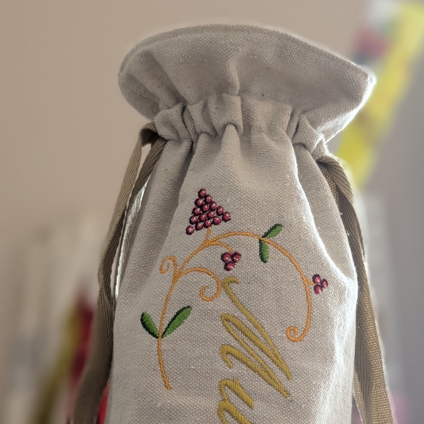 Embroidered drawstring bag with grapevine design and initials on a blurred background