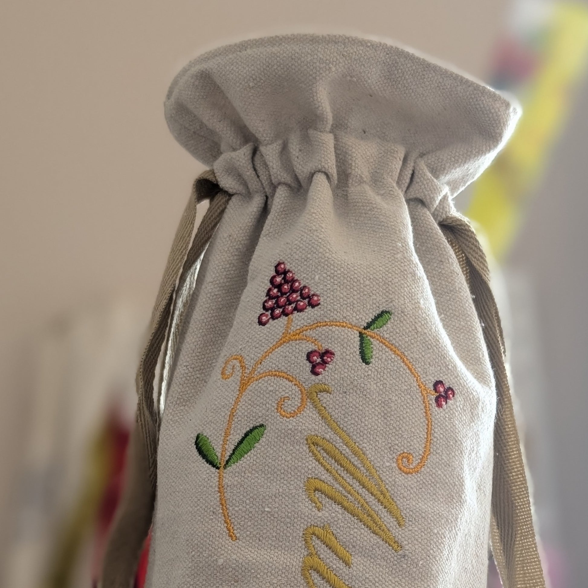Embroidered drawstring bag with grapevine design and initials on a blurred background