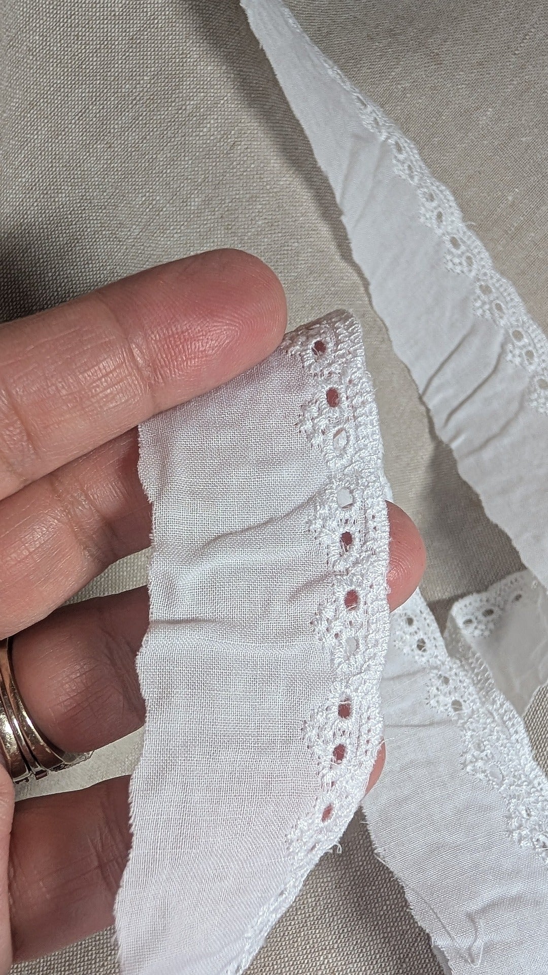 Close-up of Martha Pullen Cotton Swiss Edging in white held between fingers on a neutral background