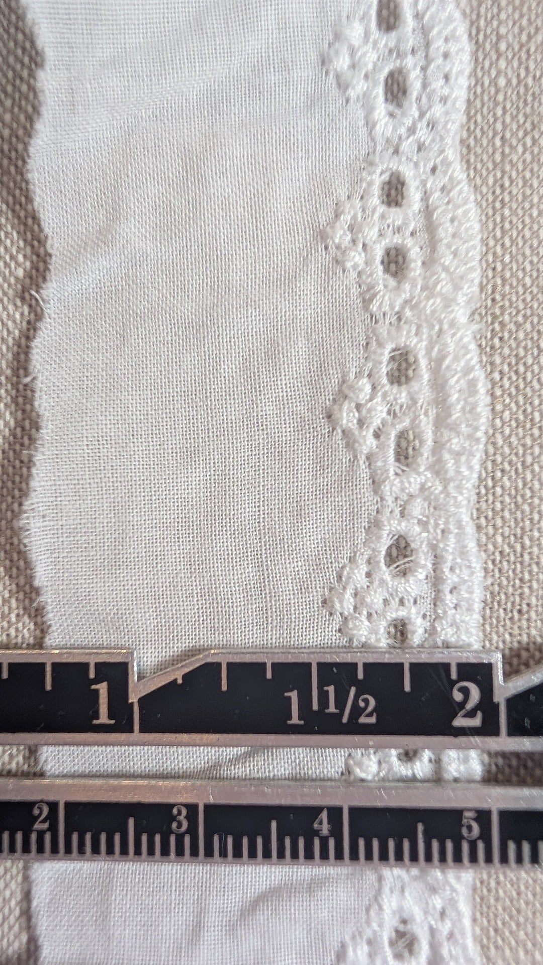 Close-up of Martha Pullen cotton Swiss embroidery lace trim with a ruler for scale on a textured fabric background