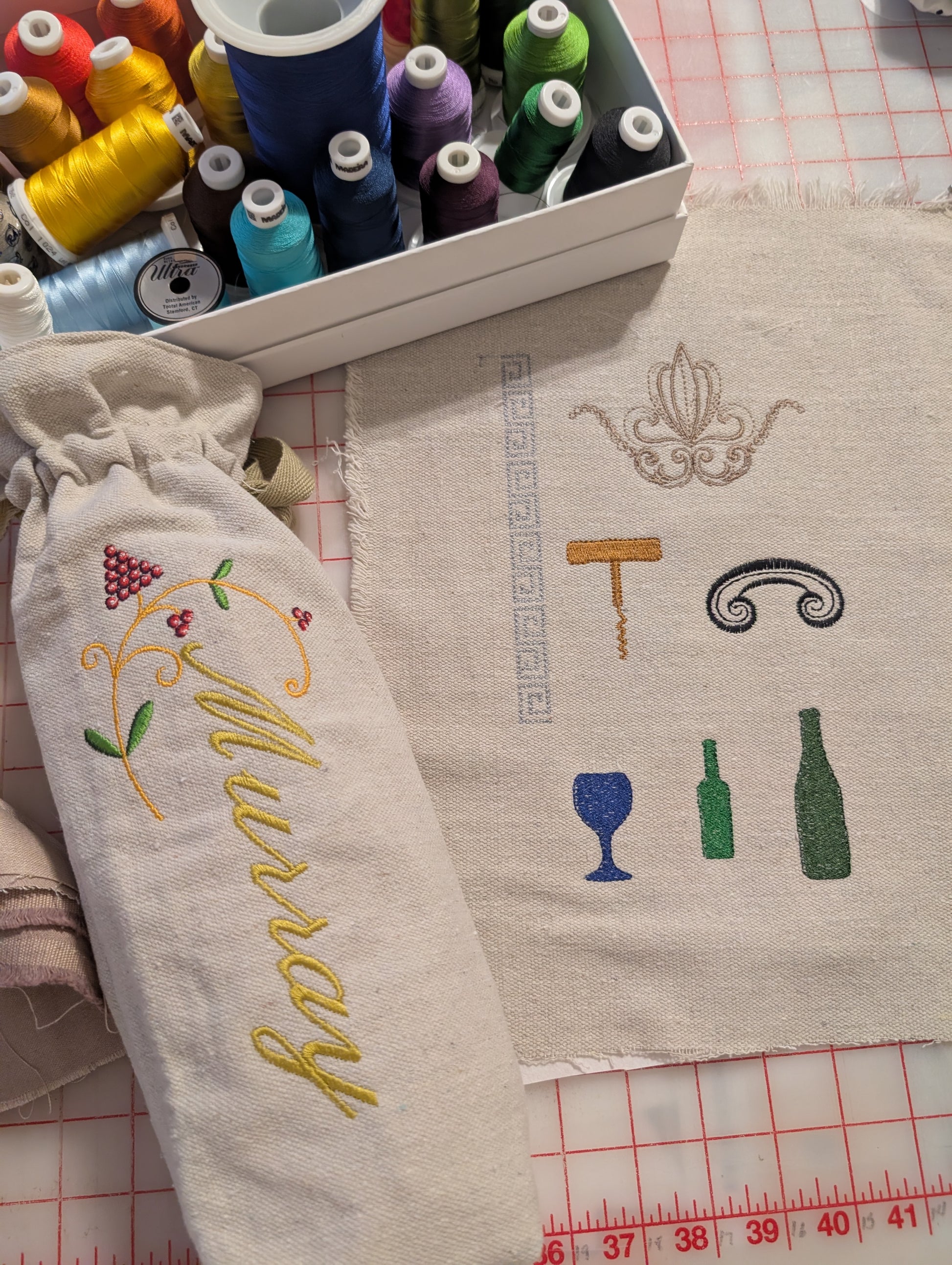 Embroidery wine gift bag with 'Murray' text and wine-themed designs on fabric, with embroidery threads in the background.