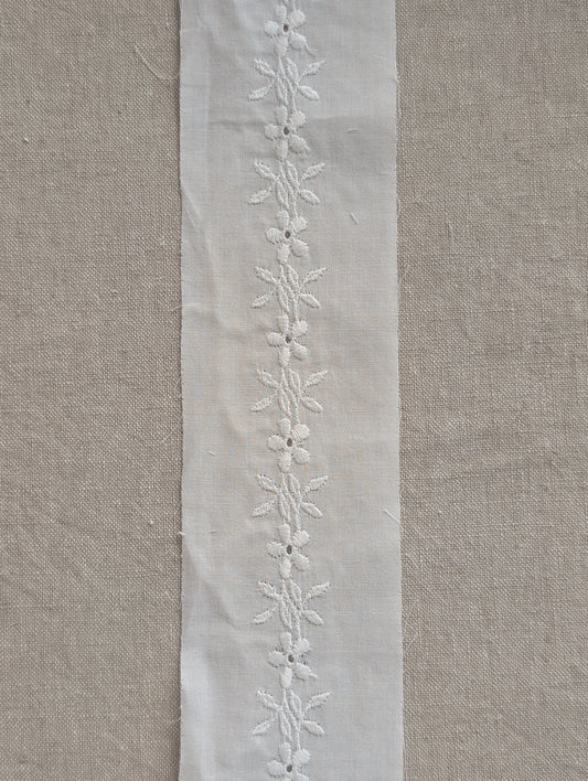 Close up cotton Swiss trim in white form Martha Pullen. It has a Floral motif vine with leaves embroidery going down the  middle. 