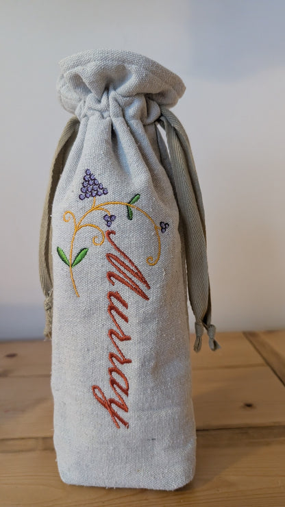 A cream-colored wine bottle bag with a drawstring closure and a tan drawstring. The bag features a gold embroidered corkscrew and the name "Murray" in gold script.