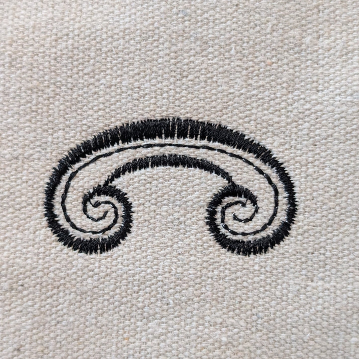 Black embroidered swirl design on a beige fabric background