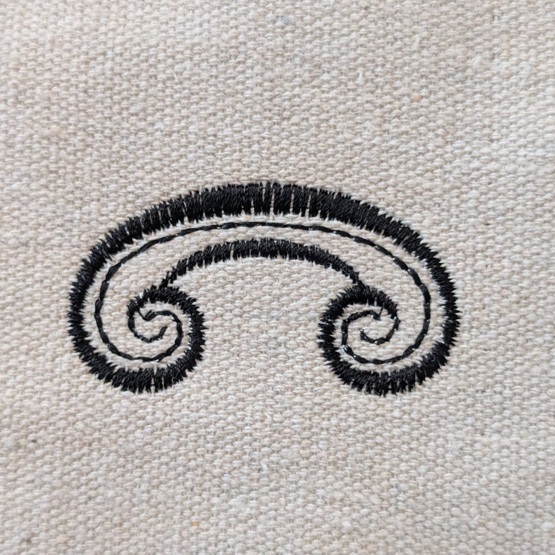 Black embroidered swirl design on a beige fabric background