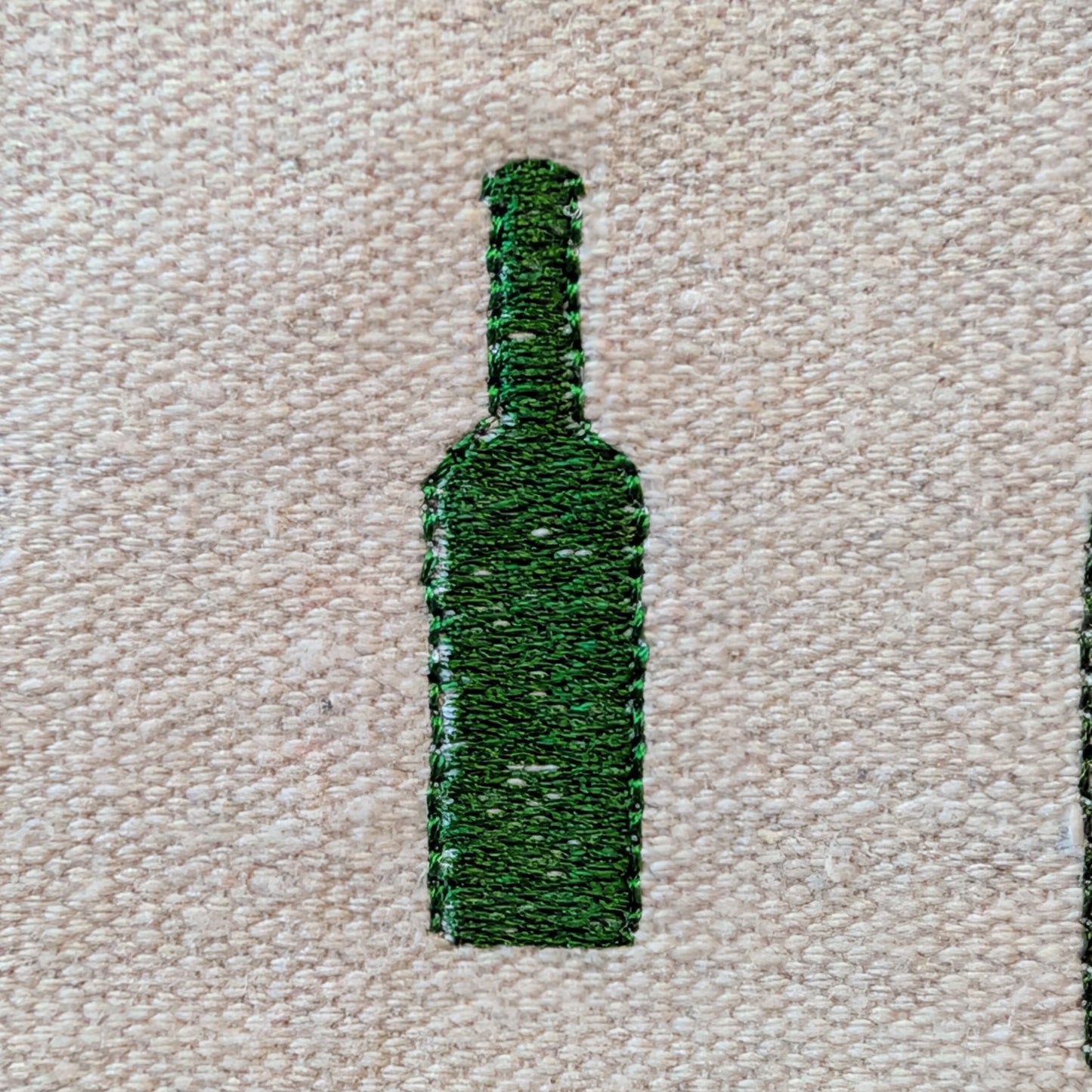 Green embroidered wine bottle design on beige fabric